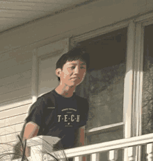 a young man wearing a t-e-c-h t-shirt stands on a balcony