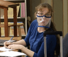 a woman wearing glasses and a face shield looks at the camera