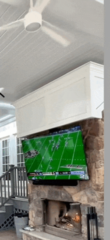 a large flat screen tv is mounted above a fireplace and shows a football game