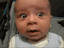 a baby with a surprised look on his face is wearing a blue vest