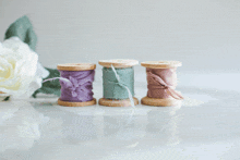 three wooden spools with purple green and pink ribbons