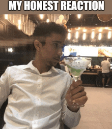 a man in a white shirt is holding a martini glass with a caption that reads my honest reaction