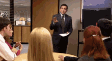 a man in a suit and tie is giving a presentation to a group of people at a table .