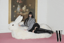 a woman is laying on a stuffed rabbit in front of a painting that says w