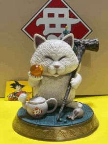 a statue of a white cat holding a ball and a teapot with a chinese symbol on it