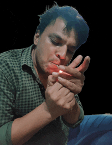 a man in a plaid shirt is lighting up a cigarette