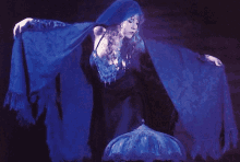 a woman in a blue cape is standing next to a blue lamp