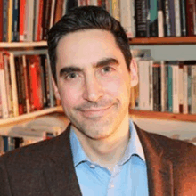 a man is smiling in front of a bookshelf filled with books .