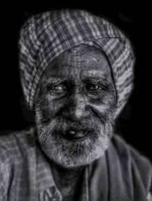 a black and white photo of an old man with a beard wearing a plaid turban