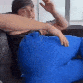 a young man is sitting on a couch with a blue pillow on his lap .