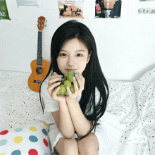 a girl holding a bunch of green grapes in front of a guitar