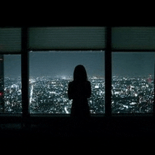 a woman is standing in front of a large window looking out over a city at night .