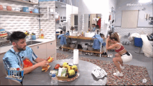 a woman squatting next to a man eating chips in a kitchen