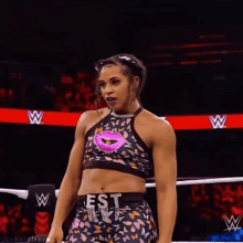 a woman is standing in a wrestling ring wearing a crop top with a pink lip on it .