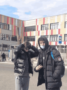 a man wearing a mask is standing next to another man in front of a bus stop