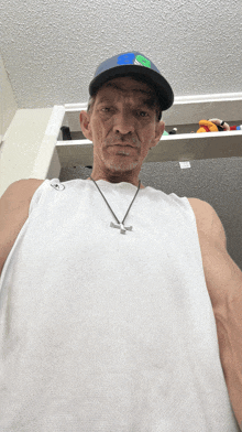 a man wearing a white tank top and a hat with a cross on it