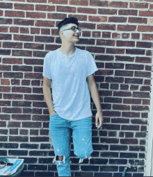 a man standing in front of a brick wall wearing a white shirt