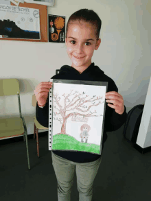 a young girl holds up a drawing of a tree with a sign that says " edición de prompta " on it