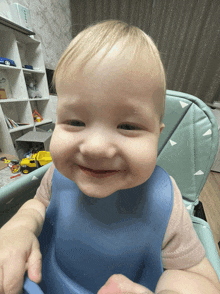 a baby wearing a blue bib is smiling and looking at the camera