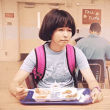 a girl sitting at a table with a tray of food in front of a sign that says fall fling