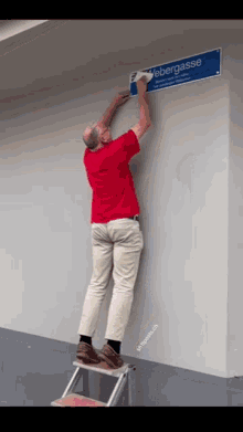 a man in a red shirt is standing on a ladder attaching a sign to a wall that says webergasse