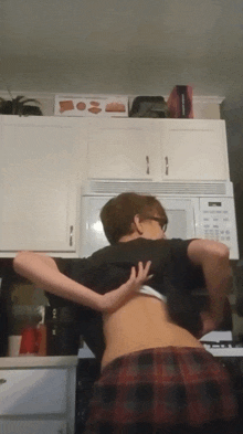 a person is taking off their shirt in front of a microwave