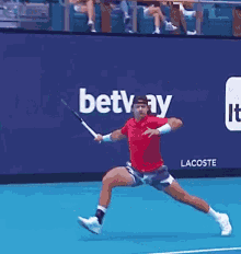 a man in a red shirt is swinging a tennis racquet on a tennis court in front of a lacoste ad