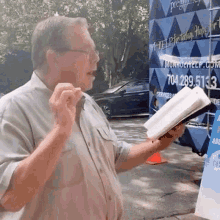 a man is holding a bible in front of a blue truck that says ' i help ' on it .