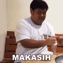 a man in a white shirt is sitting at a table with a bowl of food and the word makasih on the table