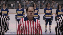 a group of hockey players are standing in a line with a referee wearing a red white and blue striped shirt .