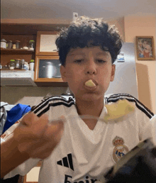 a young boy wearing a white adidas shirt is eating something