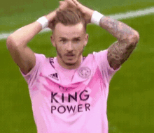 a soccer player in a pink king power jersey is holding his head .