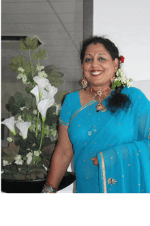 a woman in a blue sari is smiling in front of a vase of flowers