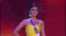 a woman in a yellow dress with a sash that says philippines on it is standing on a stage .