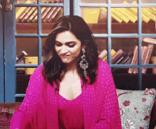 a woman in a pink dress is sitting on a couch in front of a bookshelf with books on it