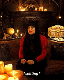 a woman in a red sweater is sitting on a couch with candles around her .