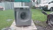 a washing machine is sitting on a wooden pallet in a backyard .