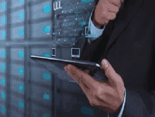 a man in a suit is holding a tablet in front of a server room .