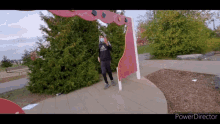 a man wearing a mask and a black adidas shirt stands in front of a red archway in a park