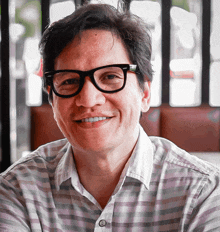 a man wearing glasses and a striped shirt is smiling