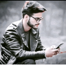 a man wearing glasses and a leather jacket is looking at his cell phone