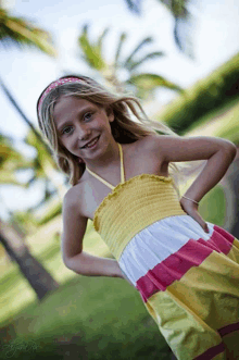 a young girl wearing a yellow and pink dress is smiling for the camera