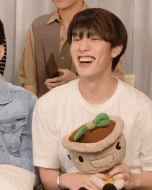 a young man is holding a stuffed animal and laughing while sitting at a table .