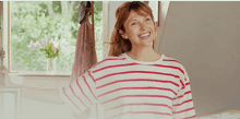 a woman in a red and white striped shirt smiles in front of a window