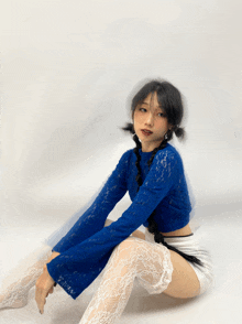 a woman wearing a blue lace top and white lace stockings sits on the floor