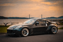 a black sports car is parked on the side of a road next to a body of water .