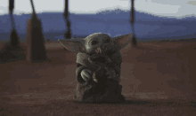 a baby yoda with a snake in its mouth standing in the desert