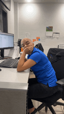 a woman in a blue shirt sits at a desk with her hand on her chin