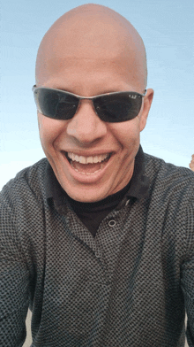 a bald man wearing sunglasses and a shirt smiles for the camera