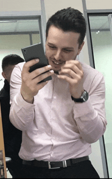 a man in a pink shirt is smiling while looking at his cell phone